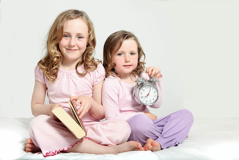 picture of 2 children on holding a book and one holding a clock
