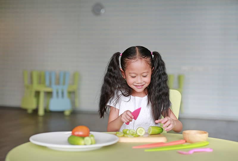 child cutting vegetables with plastic knife