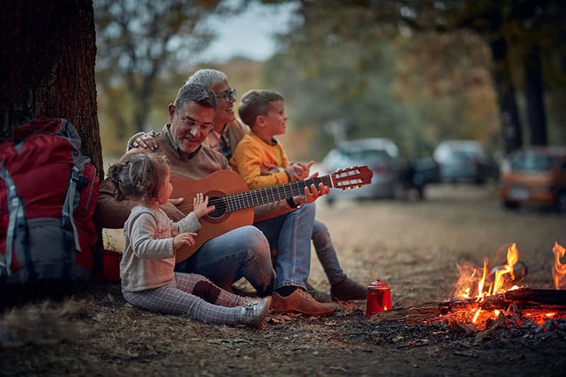 adult playing guitar for children at a campfire