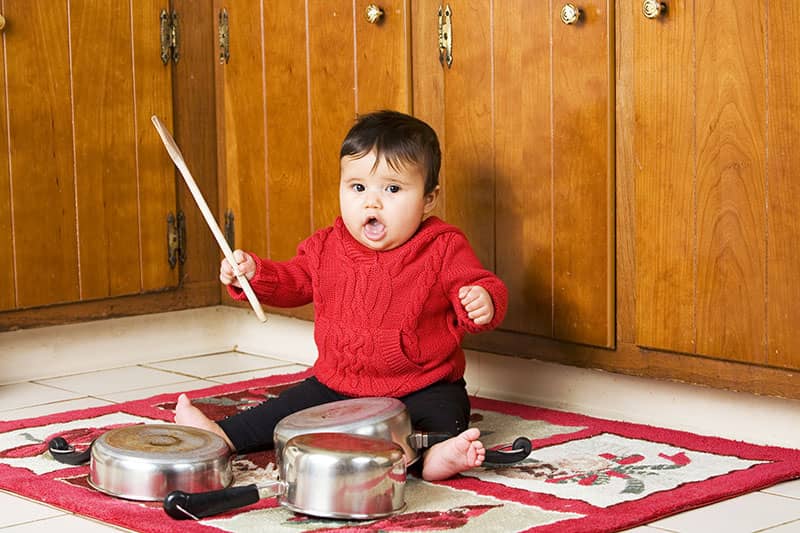 child hitting pots and pans with drumstick